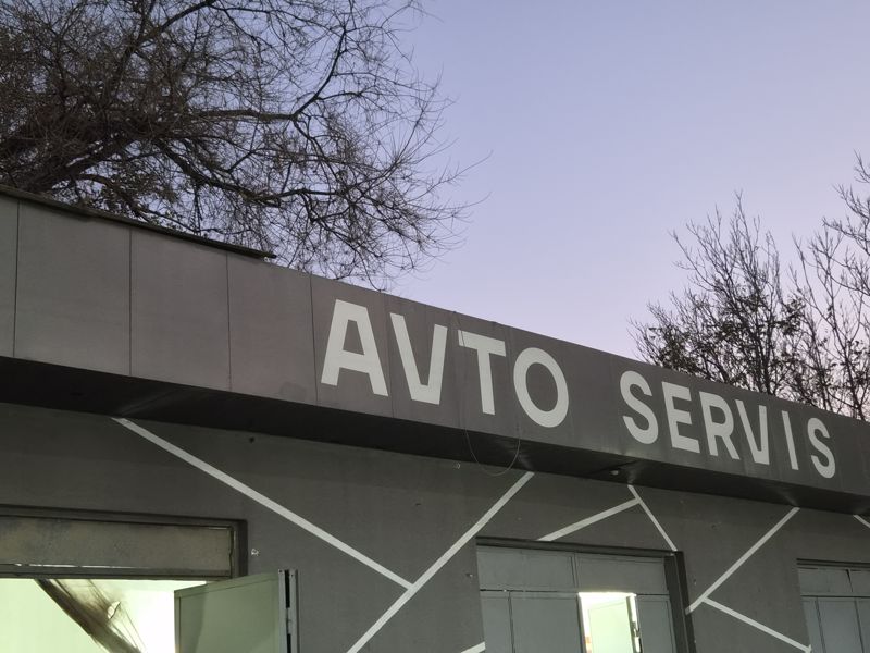 Надпись «AVTO SERVIS» на фасаде над воротами боксов, сумерки